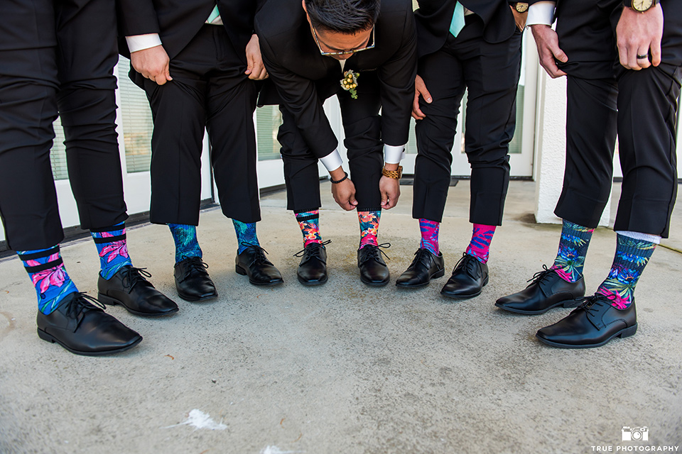  the groom in a black tuxedo with a black bow tie, the groomsmen in black tuxedos with teal bow ties