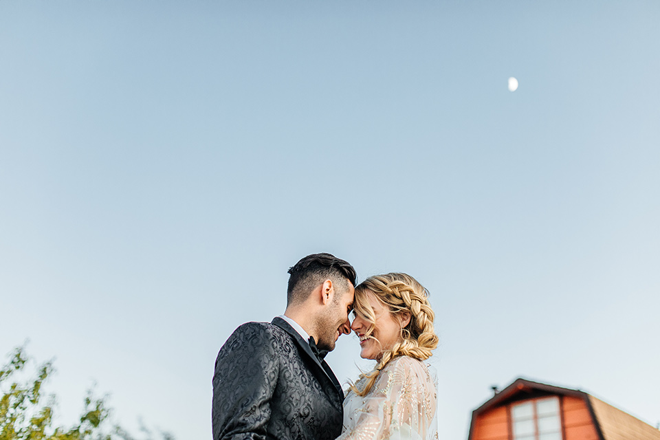  bride was in a white strapless jumpsuit with a colorful jacket and hair in a ponytail and the groom in a black paisley tuxedo with a peak lapel and black bow tie 