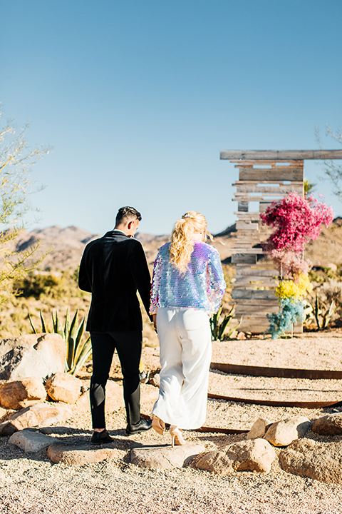  bride was in a white strapless jumpsuit with a colorful jacket and hair in a ponytail and the groom in a black paisley tuxedo with a peak lapel and black bow tie 