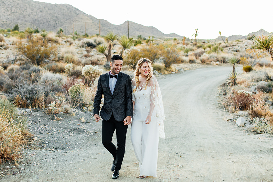  bride was in a white strapless jumpsuit with a colorful jacket and hair in a ponytail and the groom in a black paisley tuxedo with a peak lapel and black bow tie 