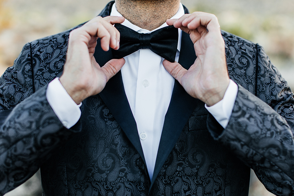  the groom in a black paisley tuxedo with a peak lapel and black bow tie 