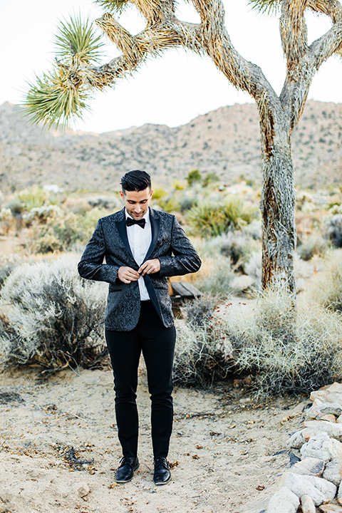  the groom in a black paisley tuxedo with a peak lapel and black bow tie 