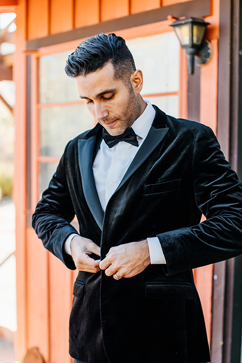  the groom in a black velvet tuxedo with a peak lapel and black bow tie 