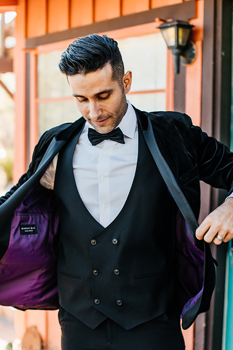  the groom in a black velvet tuxedo with a peak lapel and black bow tie 