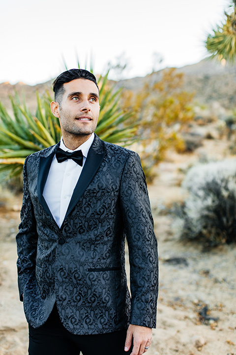  the groom in a black paisley tuxedo with a peak lapel and black bow tie 