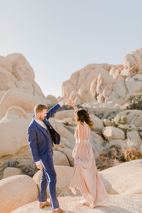  bride in a taupe colored maxi dress with straps and her hair down the groom in a cobalt blue suit with a neutral colored tie, dancing 