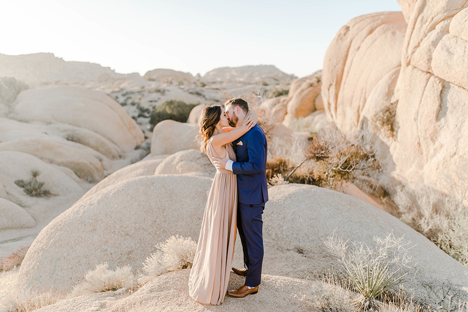  bride in a taupe gown with ankle boots and straps, the groom in a cobalt blue suit with a neutral colored tie kissing