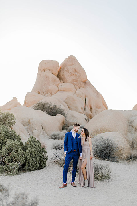  bride in a taupe colored maxi dress with straps and her hair down the groom in a cobalt blue suit with a neutral colored tie, looking at each other 