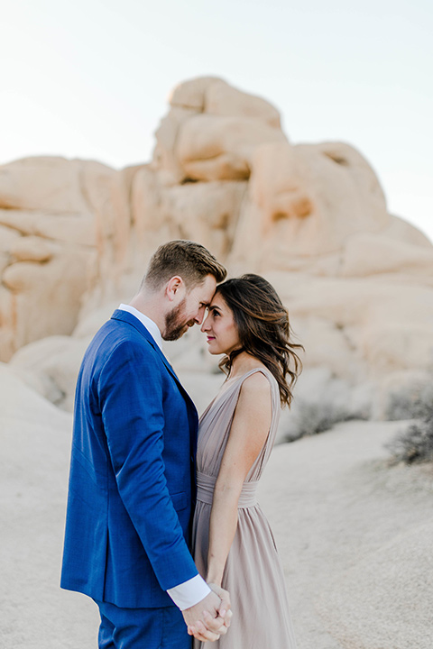  bride in a taupe colored maxi dress with straps and her hair down the groom in a cobalt blue suit with a neutral colored tie, looking at each other and touching heads 