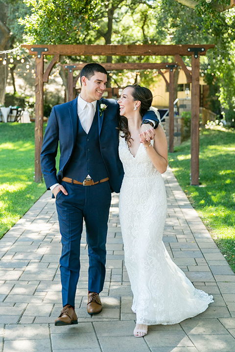  bride in a lace form-fitting gown with straps, the groom in a dark blue suit with a white long tie 