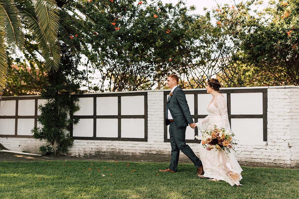 bride in a lace bohemian gown with a high neckline and flutter sleeves, the groom was in grey retail suit with a blue long tie, walking on grass