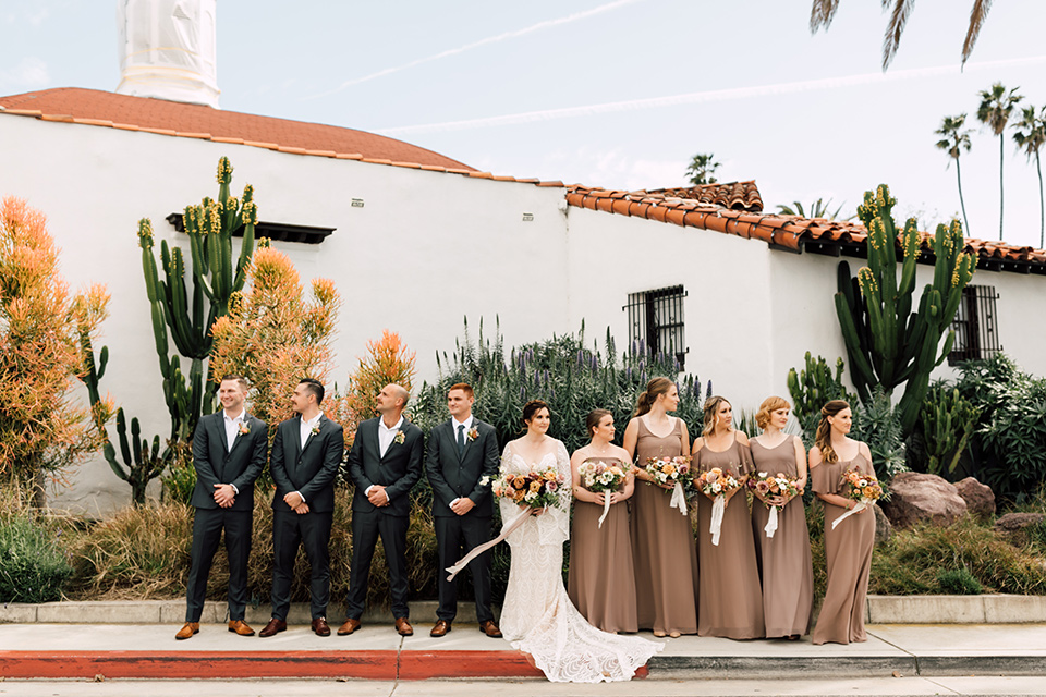 bride in a lace bohemian gown with a high neckline and flutter sleeves, the groom was in grey retail suit with a blue long tie, the bridesmaids in taupe neutral gowns and the groomsmen in grey suits for purchase with blue long ties