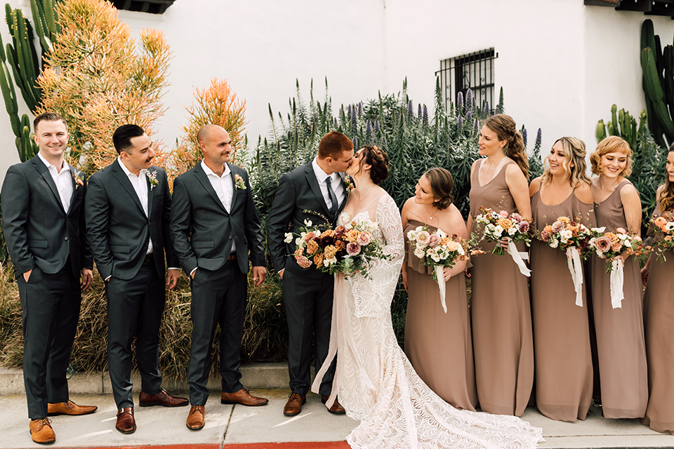 bride in a lace bohemian gown with a high neckline and flutter sleeves, the groom was in grey retail suit with a blue long tie, the bridesmaids in taupe neutral gowns and the groomsmen in grey suits for purchase with blue long ties