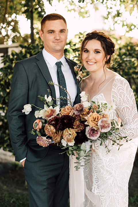 bride in a bohemian style gown with lace, a high neckline, and flutter sleeves, and the groom in a grey suit with a blue long tie
