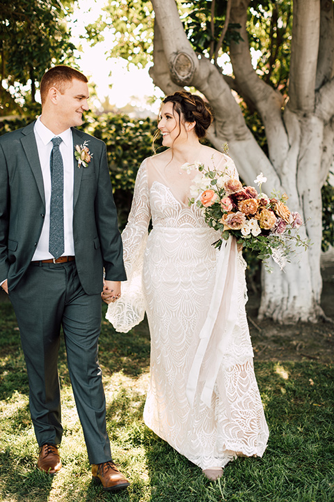 bride in a bohemian style gown with lace, a high neckline, and flutter sleeves groom in a grey suit with a blue long tie