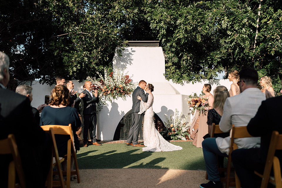 bride in a lace bohemian gown with a high neckline and flutter sleeves, the groom was in grey retail suit with a blue long tie, at the ceremony