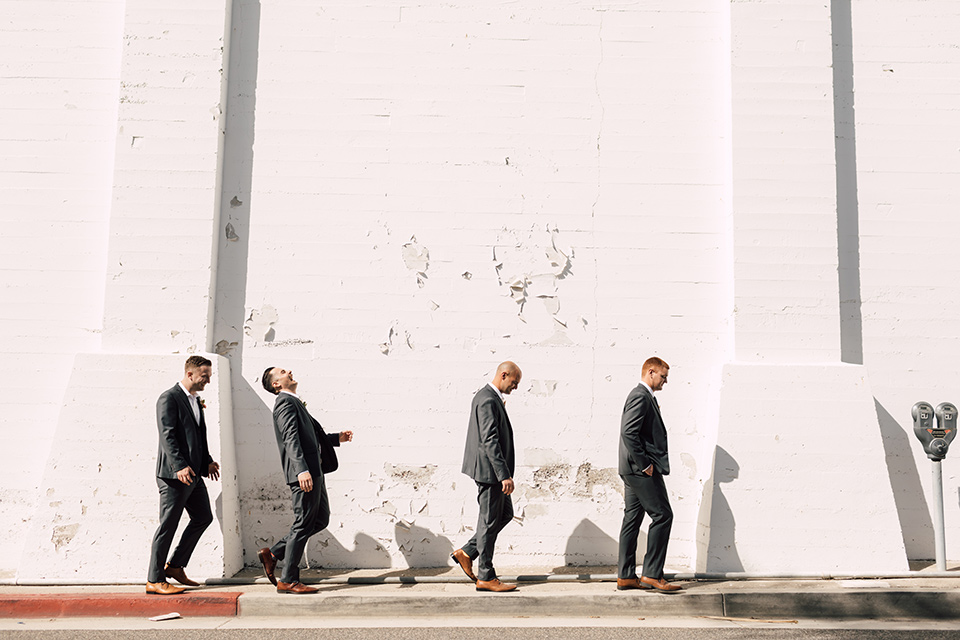 groom and groomsmen in grey suits walking by white brick wall