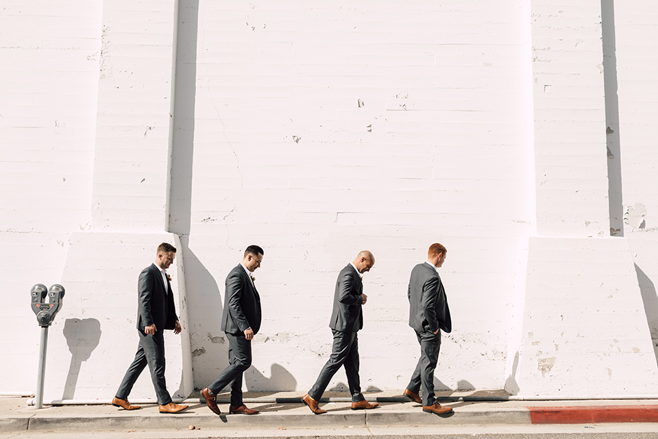groom and groomsmen in grey suits walking by white brick wall