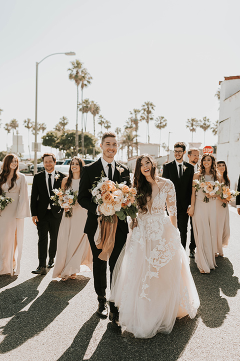  bride in a flowing ballgown and the groom in a black suit, the bridesmaids in neutral colors and the groomsmen in black suits and long ties 