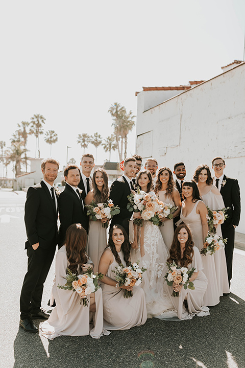  bride in a flowing ballgown and the groom in a black suit, the bridesmaids in neutral colors and the groomsmen in black suits and long ties 