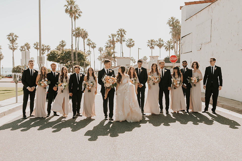  bride in a flowing ballgown and the groom in a black suit, the bridesmaids in neutral colors and the groomsmen in black suits and long ties 