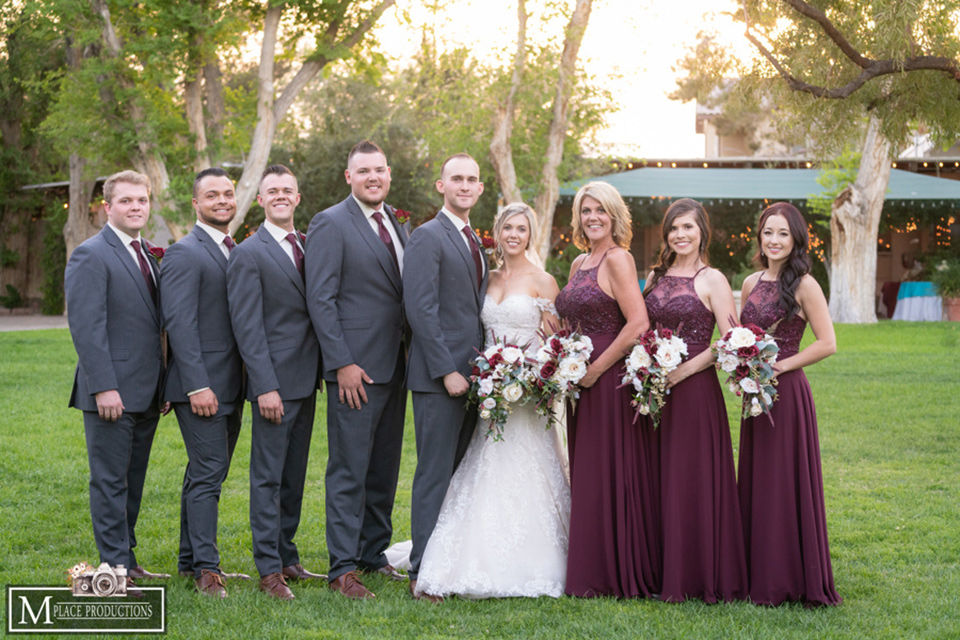  bride in a white lace gown with an off the shoulder detail and long veil and the groom in a dark grey suit and the bridesmaids in burgundy long dresses and the groomsmen in a charcoal grey suits and burgundy long tie