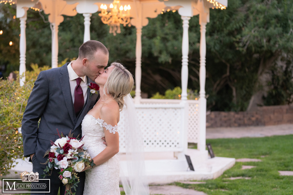  bride in a white lace gown with an off the shoulder detail and long veil and the groom in a dark grey suit kissing