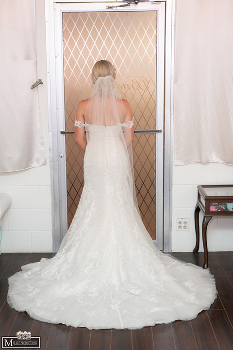  bride in a white lace gown with an off the shoulder detail and long veil and the groom in a dark grey suit 