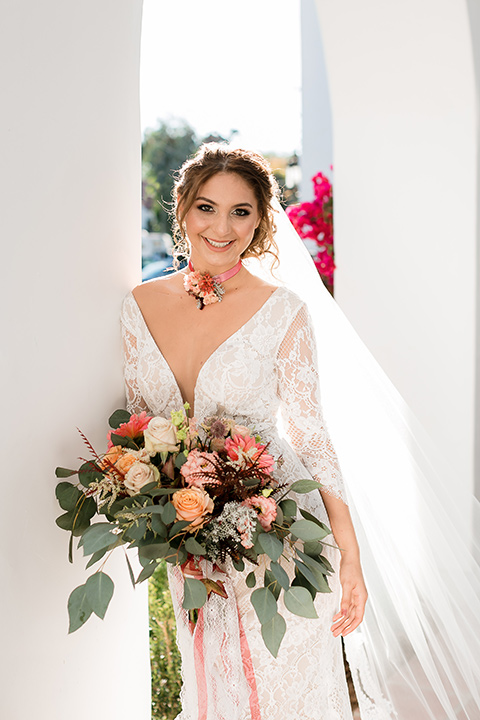  the bride in a lace formfitting gown with sleeves and a floral necklace