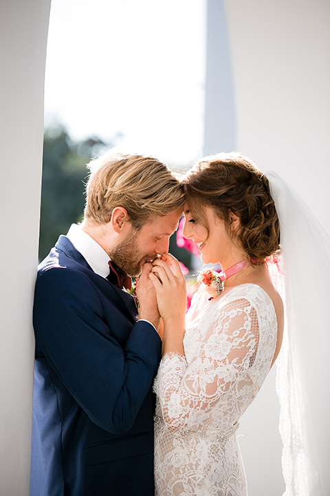 bride in a Spanish lace formfitting gown with sleeves and the groom in a dark blue suit with a burgundy bow tie kissing