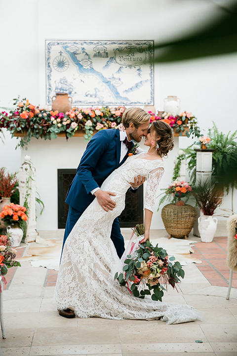 bride in a Spanish lace formfitting gown with sleeves and the groom in a dark blue suit with a burgundy bow tie