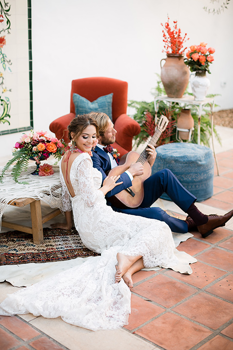 bride in a Spanish lace formfitting gown with sleeves and a floral necklace, the groom in a dark blue suit in a burgundy bow tie