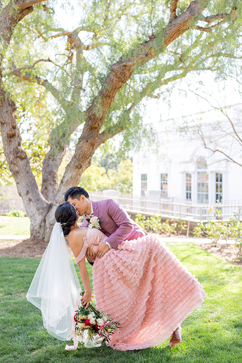  bride in a pink gown with ruffles and the groom in a rose pink suit and a pink bow tie, kissing