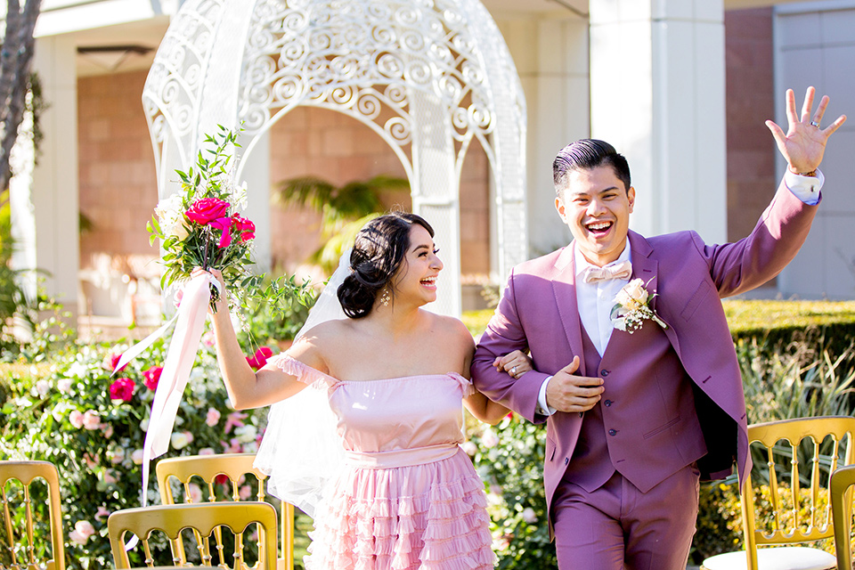  bride in a pink ballgown with ruffles and strapless neckline and the groom in a rose pink suit with a pink bow tie