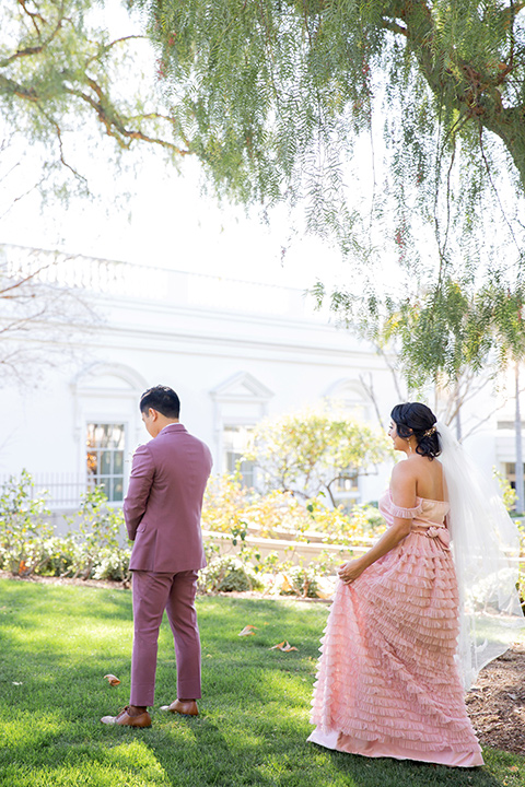  bride in a pink gown with ruffles and the groom in a rose pink suit and a pink bow tie, kissing