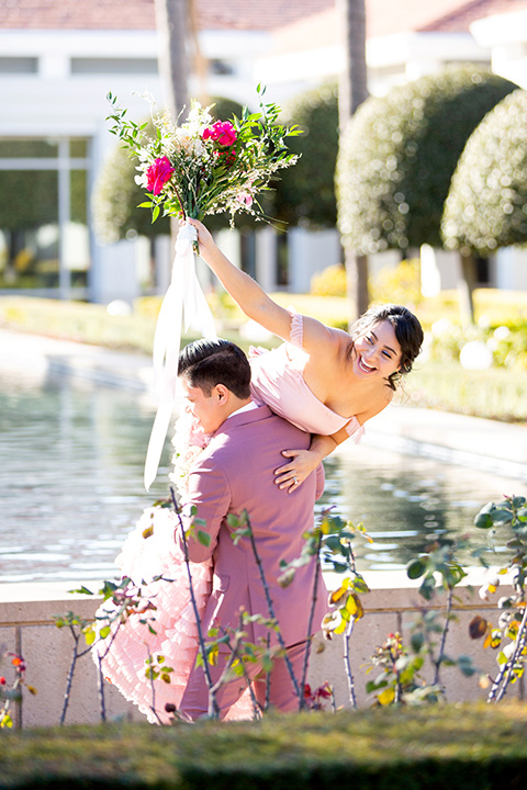  bride in a pink ballgown with ruffles and the groom in a rose pink suit with a pink bow tie