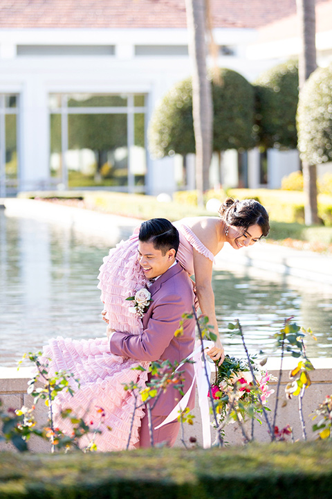  bride in a pink gown with ruffles and the groom in a rose pink suit and a pink bow tie, kissing