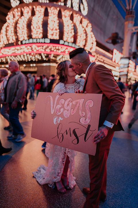  bride in a bohemian white gown with lace detailing and long sleeves and the groom in a caramel rust suit color with a brown long tie, dancing on freemont street