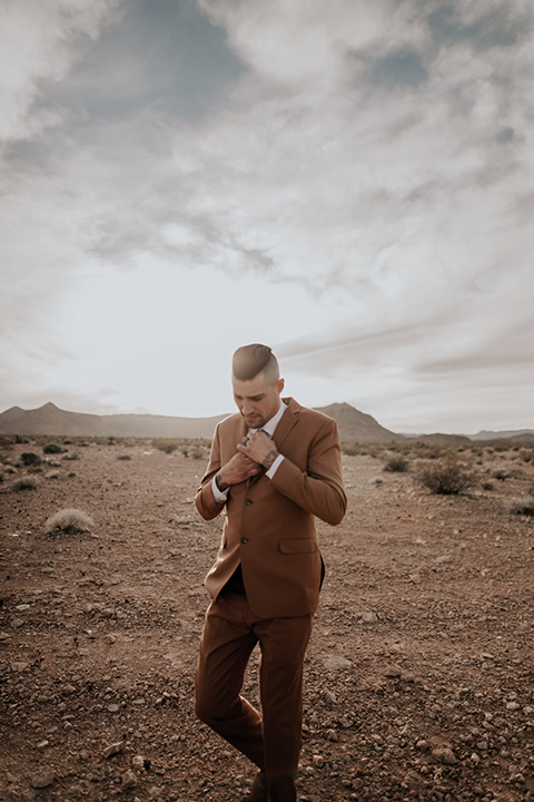  the groom in a caramel rust suit color with a brown long tie walking 