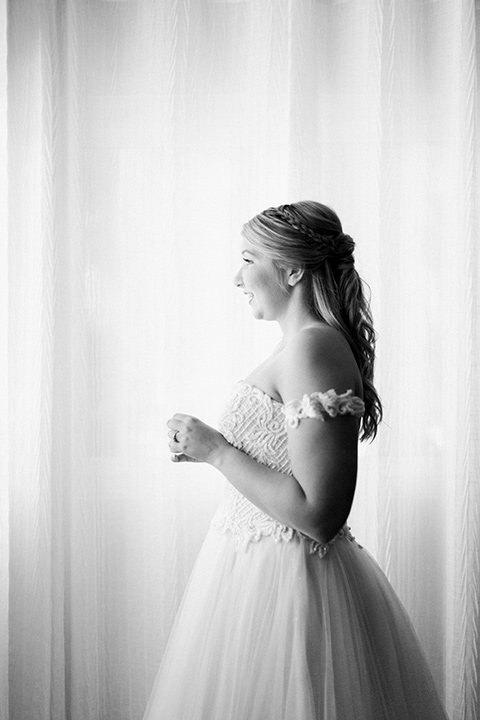  bride in a white ballgown with an off the shoulder detail looking out the window 