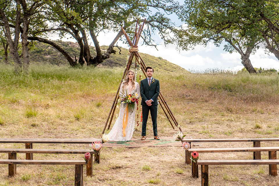  the groom in a dark green suit and brown long tie and bride in a lace gown with long sleeves 