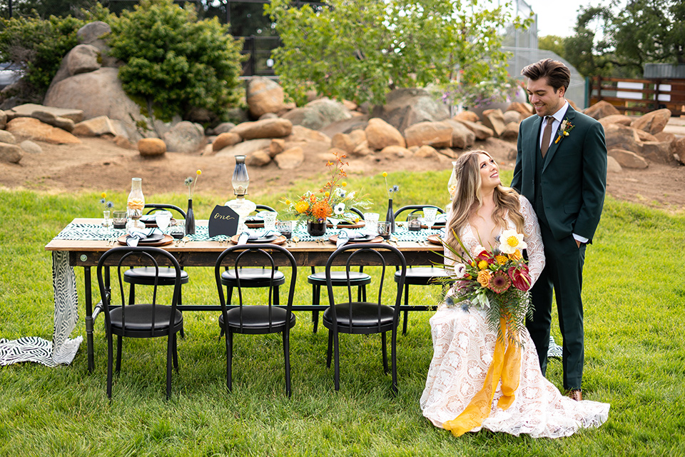  the groom in a dark green suit and brown long tie and bride in a lace gown with long sleeves 