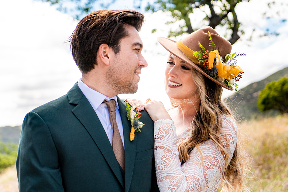  the groom in a dark green suit and brown long tie and bride in a lace gown with long sleeves 