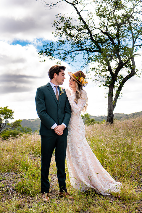  the groom in a dark green suit and brown long tie and bride in a lace gown with long sleeves 