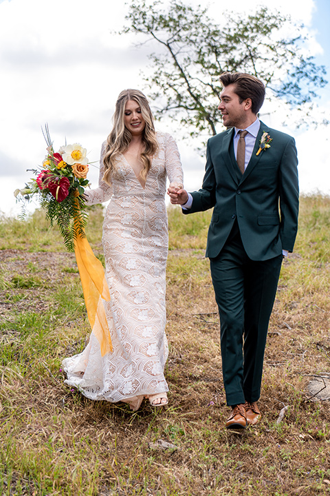  the groom in a dark green suit and brown long tie and bride in a lace gown with long sleeves 