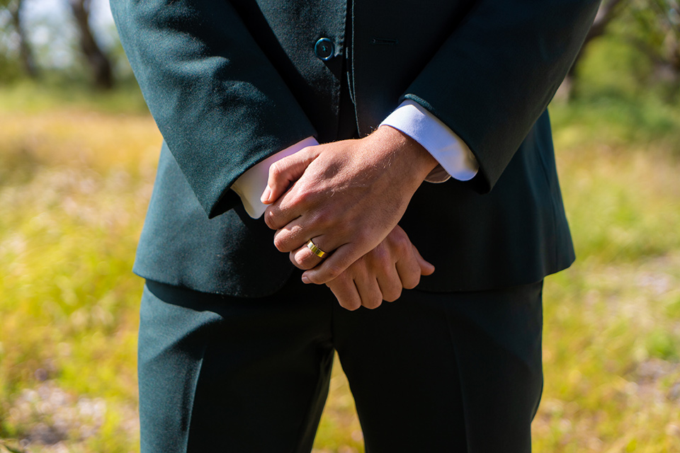  the groom in a dark green suit and brown long tie and bride in a lace gown with long sleeves 