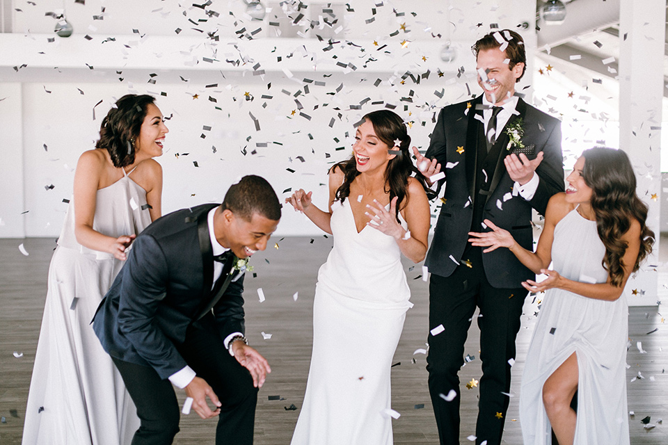  bride in a lace white gown with a long veil and the groom in a navy shawl lapel tuxedo with black bow ties, and the bridesmaid in a silver long gown and the groomsmen in a navy shawl lapel tuxedo with a black bow tie