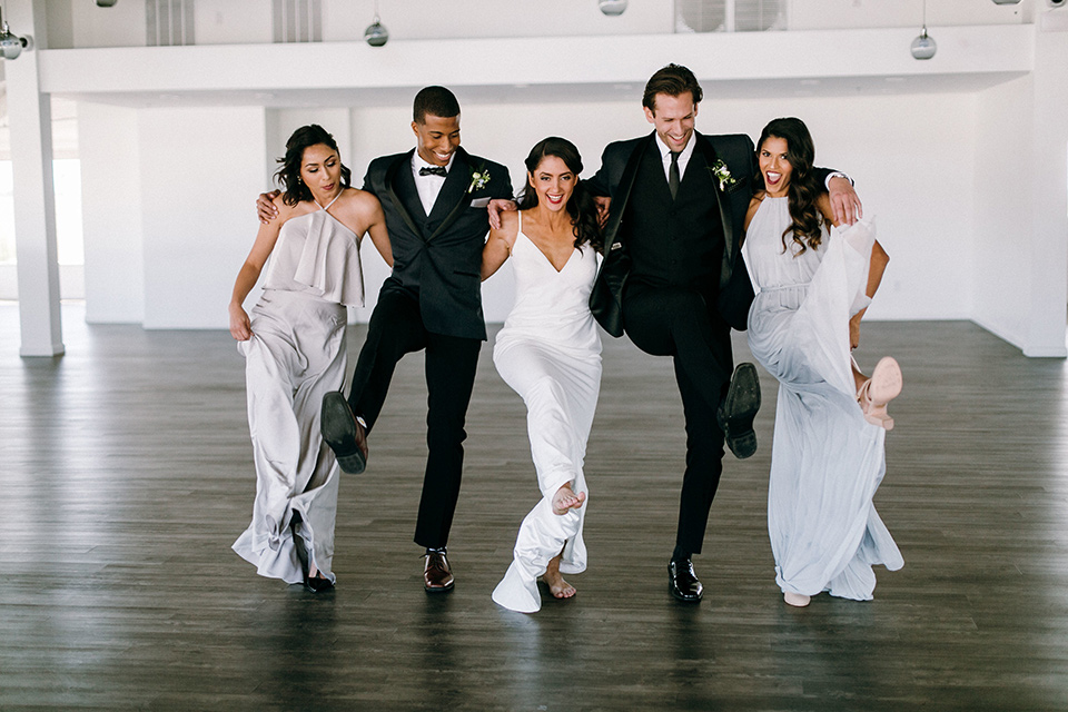  bride in a lace white gown with a long veil and the groom in a navy shawl lapel tuxedo with black bow ties, and the bridesmaid in a silver long gown and the groomsmen in a navy shawl lapel tuxedo with a black bow tie