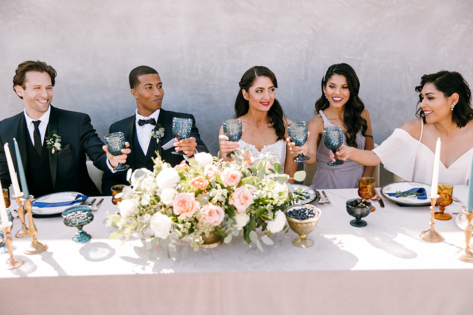  bride in a lace white gown with a long veil and the groom in a navy shawl lapel tuxedo with black bow ties, and the bridesmaid in a silver long gown and the groomsmen in a navy shawl lapel tuxedo with a black bow tie