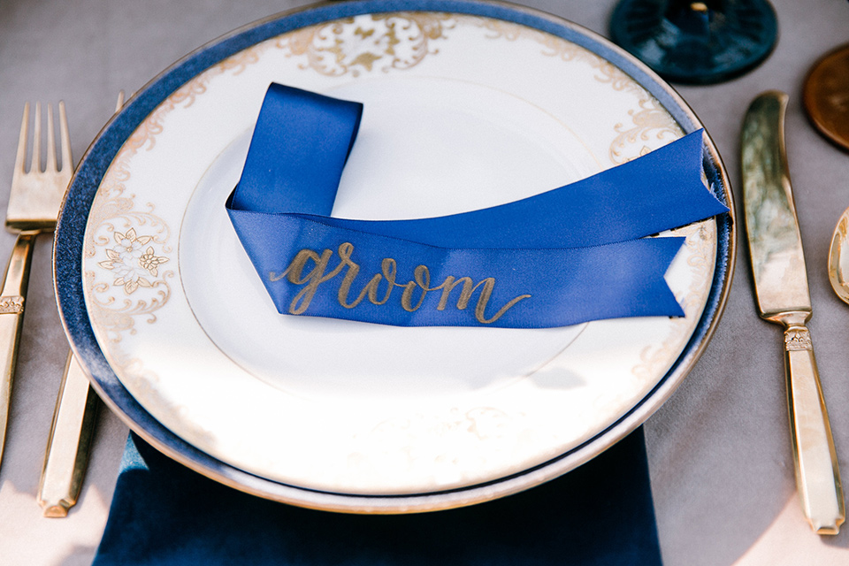  white plates and gold flatware with blue linens